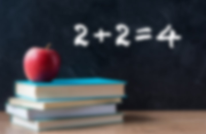 blurred stack of books with an apple on top with a blurred chalkboard in the background, demonstrating astigmatism