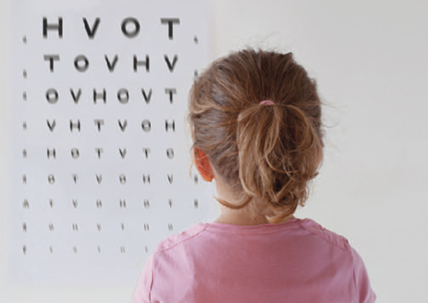 young girl looking at an early-childhood version of a Snellen chart, which has only the letters H, V, O and T.