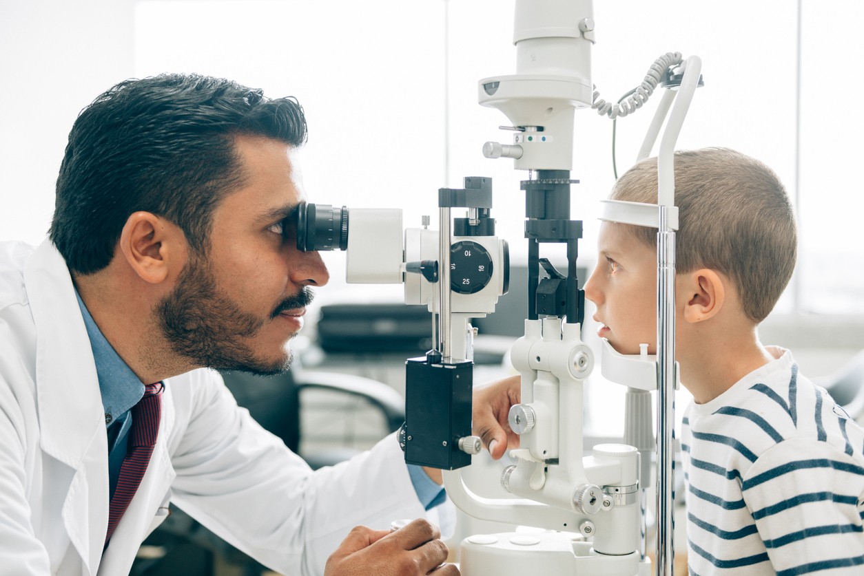 Young boy at Ophthalmologist for an eye check-up. Doctor looking into boys eyes with vision examination equipment.